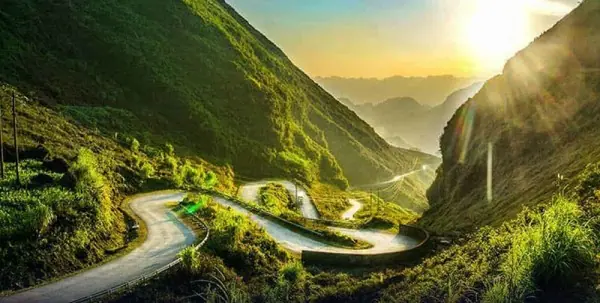 A mountain road twisting through the green valleys of Ha Giang at sunset